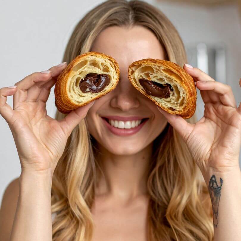 15 Cornetti proteici ripieni alla nocciola mostrati da una donna felice con un sorriso, dolcezza senza zuccheri aggiunti.