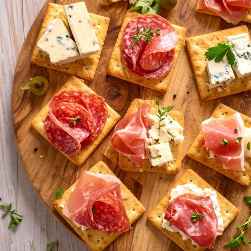 Crackers keto classici con salumi e formaggi su un tagliere in legno, ideale per la dieta chetogenica.