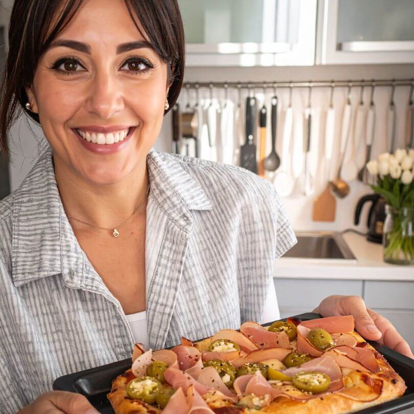 Donna sorridente che presenta una pinsa con ingredienti freschi, ideale per la dieta chetogenica e gli alimenti proteici.