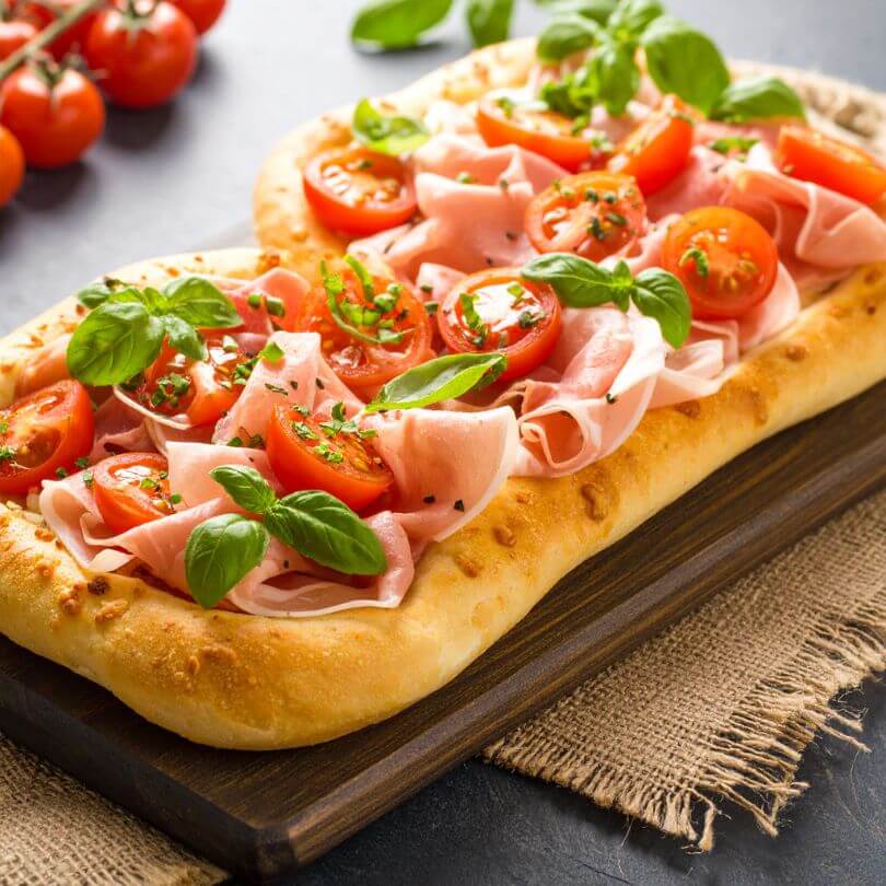 Pinsa proteica con pomodorini, prosciutto e basilico, ideale per dieta chetogenica e alimenti proteici.