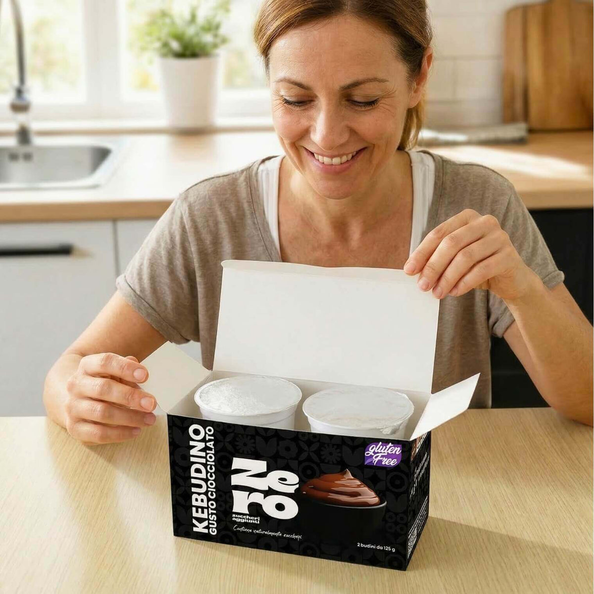Donna felice apre una confezione di Kebudino proteico al cioccolato sul tavolo, ideale per dieta chetogenica.